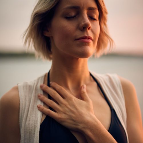 woman in white vest and black bikini with hand on chest